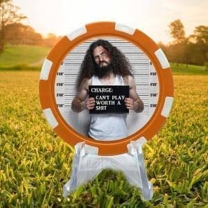 Poker chip style golf ball marker featuring an orange and white border and a mugshot of an angry looking man with long curly hair and a beard holding a sign that says "charge: can't play worth a shit."