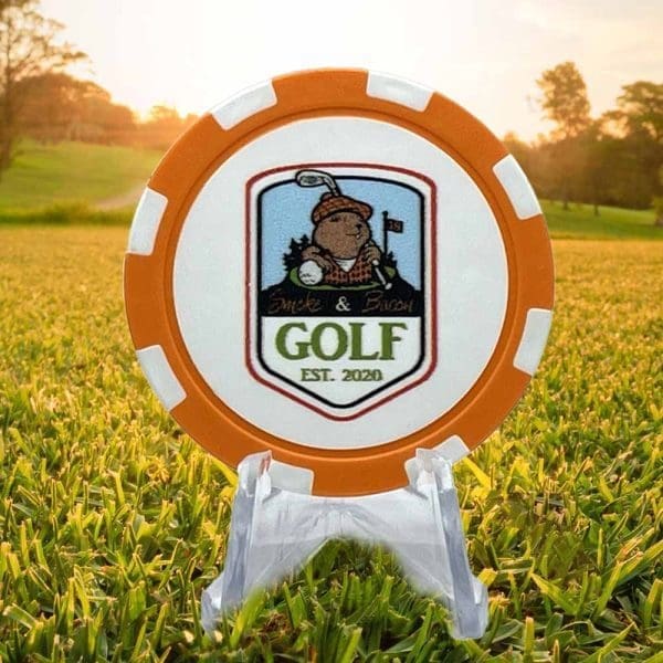 Smoke and Bacon Golf Marker Poker chip style golf ball marker featuring an orange and white border with the Smoke & Bacon Golf logo in the center against a white background.