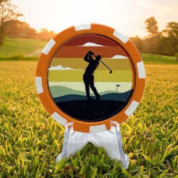 Poker chip style golf ball marker featuring an orange and white border and a silhouette of a golfer against a sunset background.
